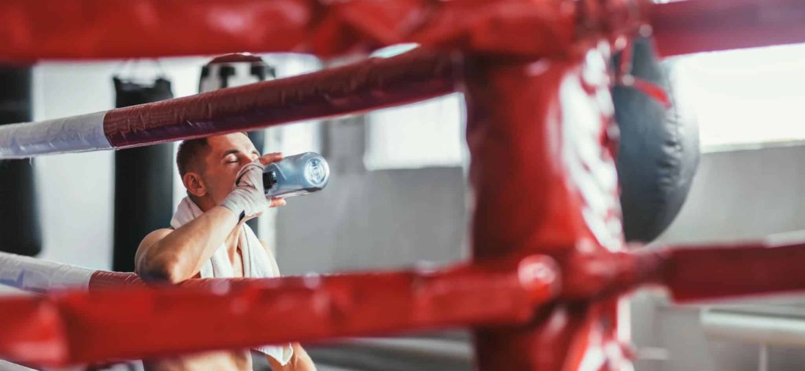 Boxer sits thoughtfully in the ring and drinks water