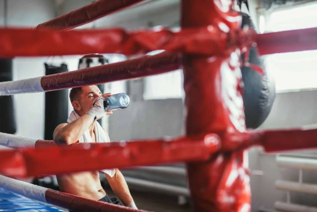 Boxer sitzt nachdenklich im Ring und trinkt Wasser